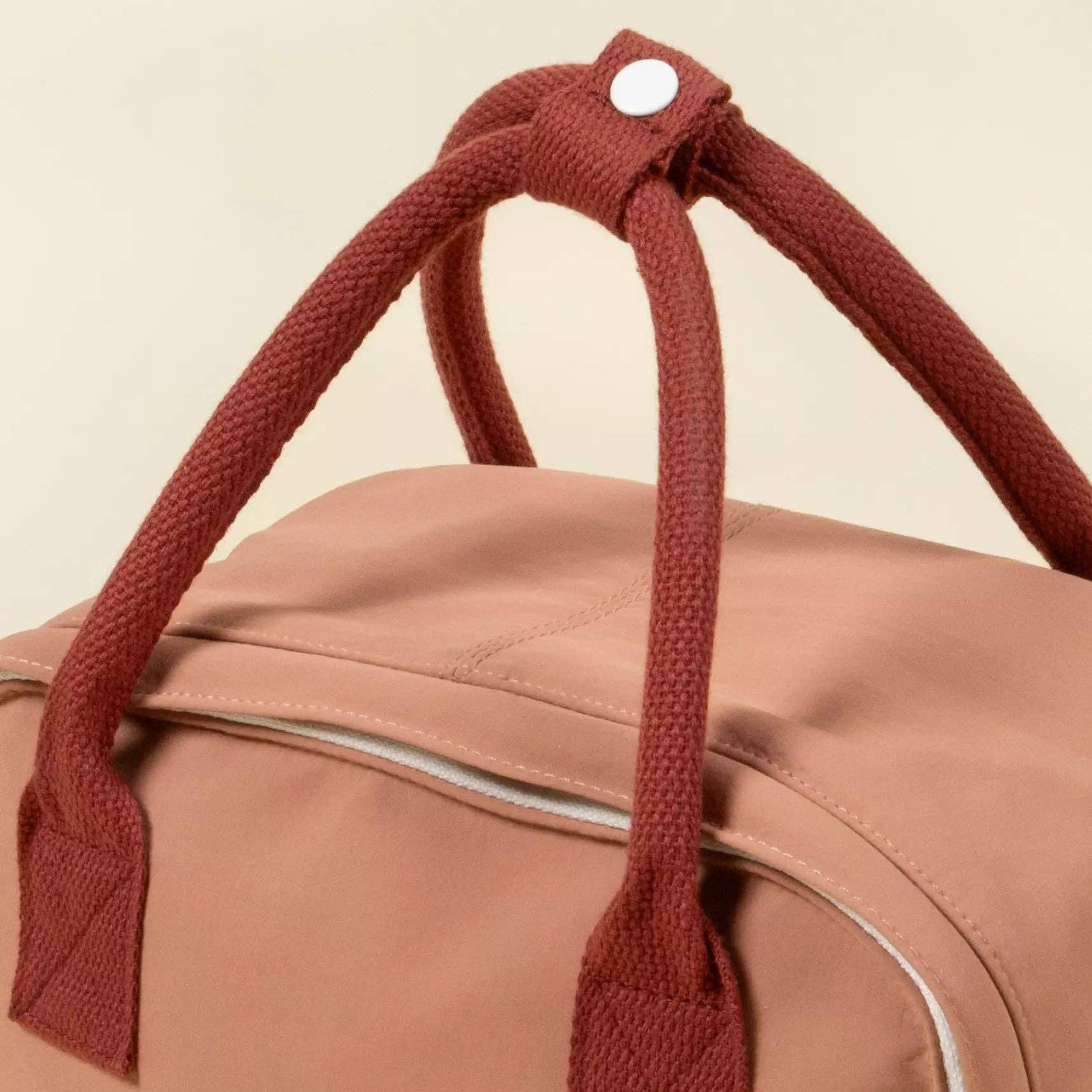 Brown duffel bag with knotted brown handles on a beige background