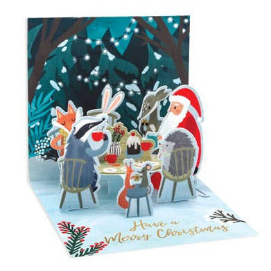Christmas card with Santa and reindeer at a table in a snowy scene
