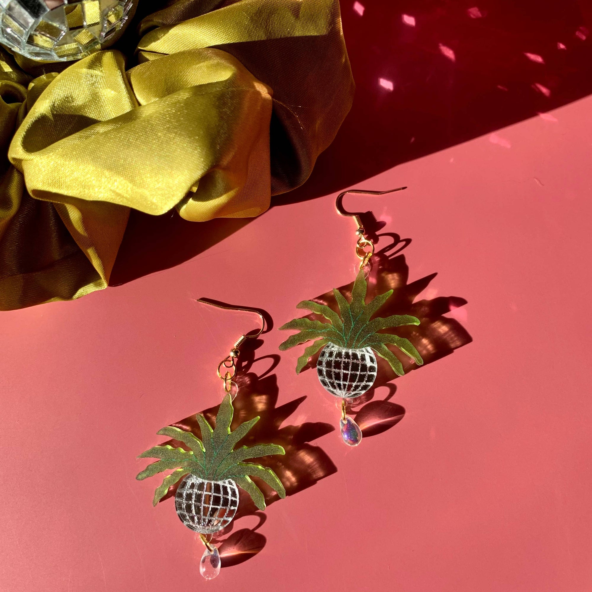 Pineapple-shaped earrings with disco ball details on a pink background