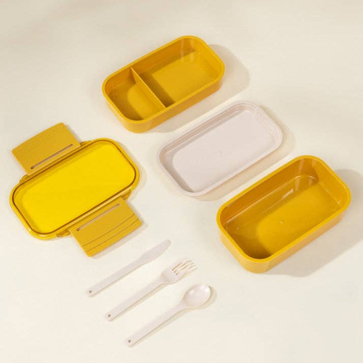 Set of yellow and beige food containers with cutlery on a light background