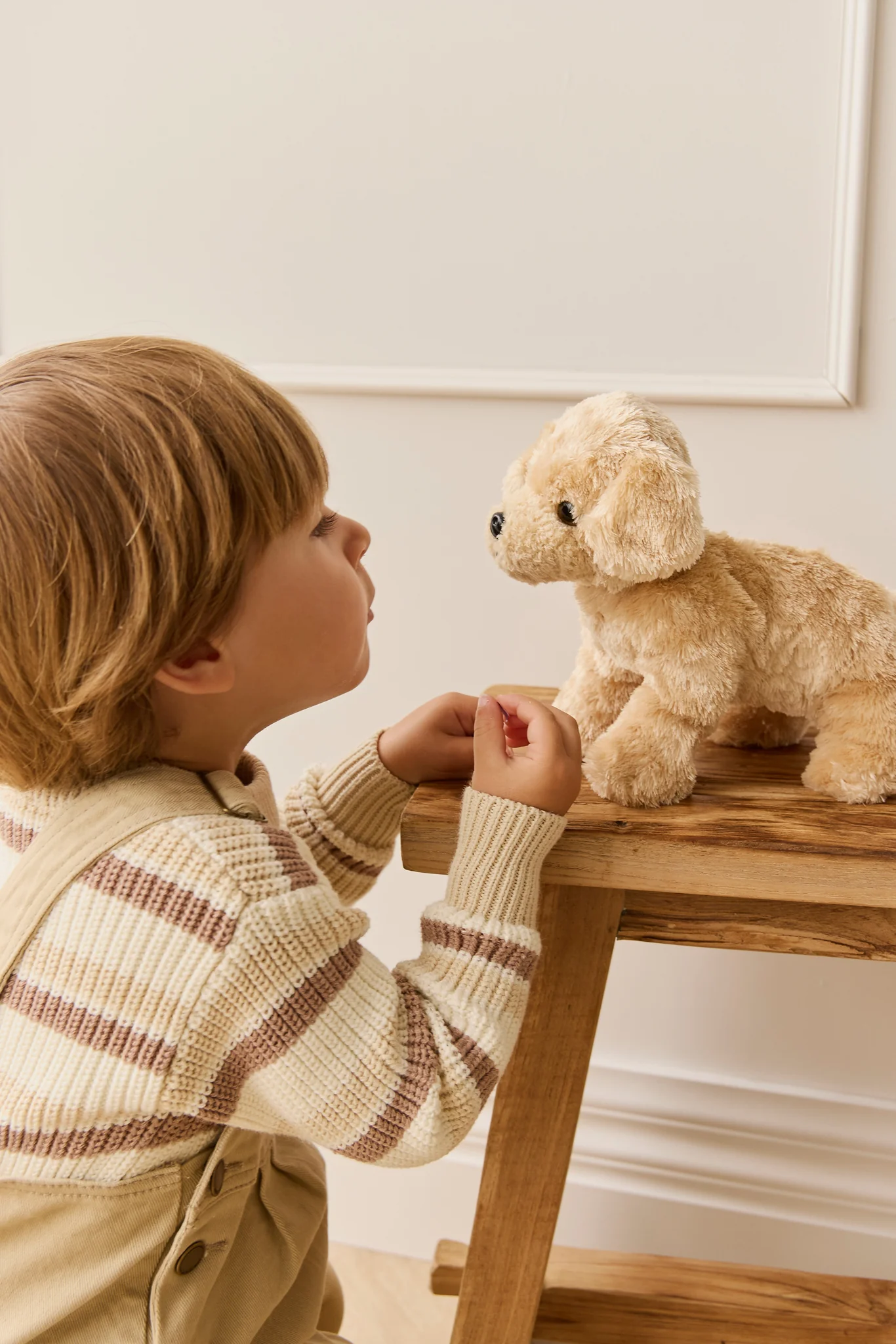 Child interacting with a teddy bear on a small wooden table.