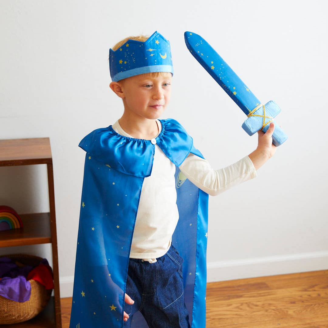 Child in a blue prince costume holding a toy sword indoors.
