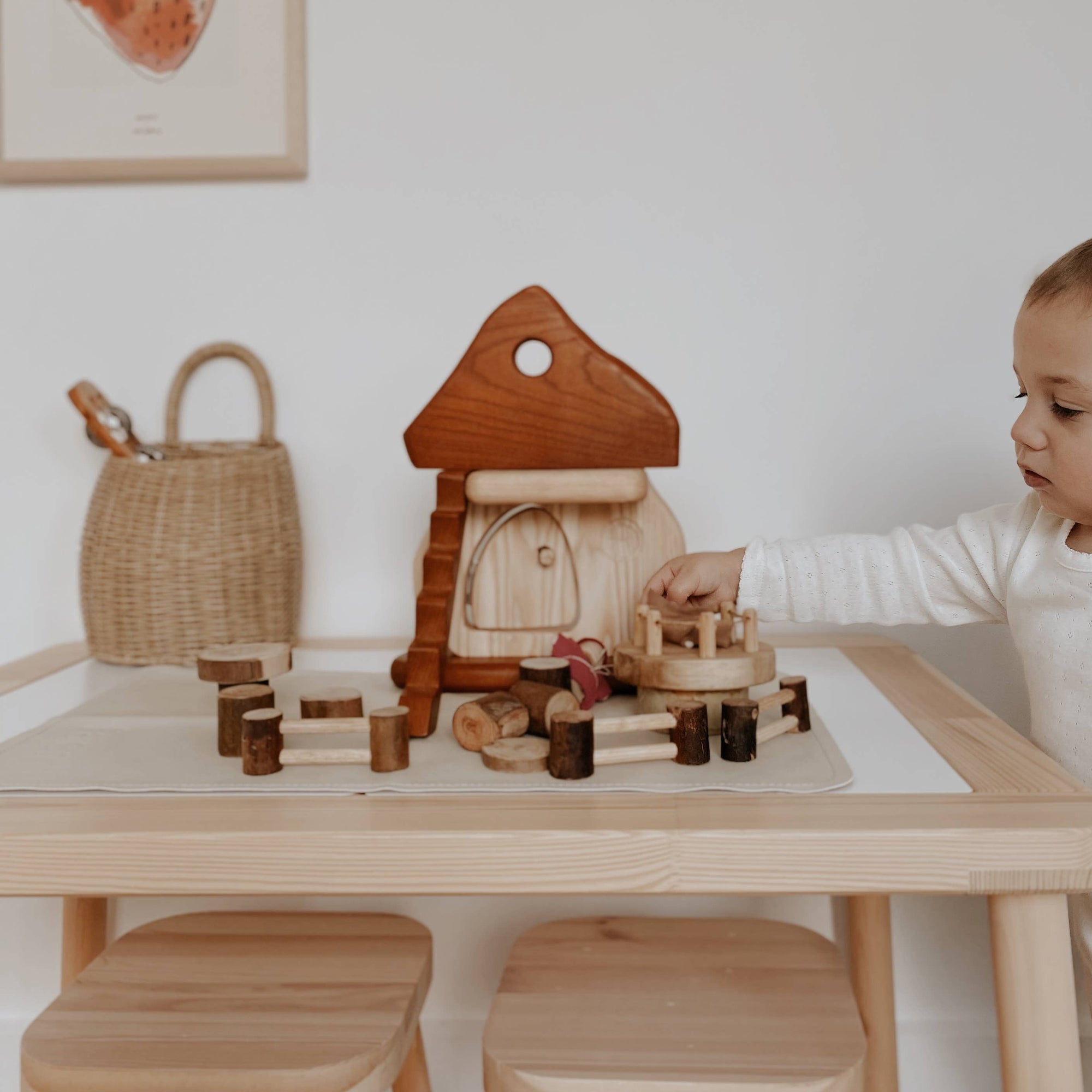 Child playing with wooden toys at a table in a room with a framed picture on the wall.
