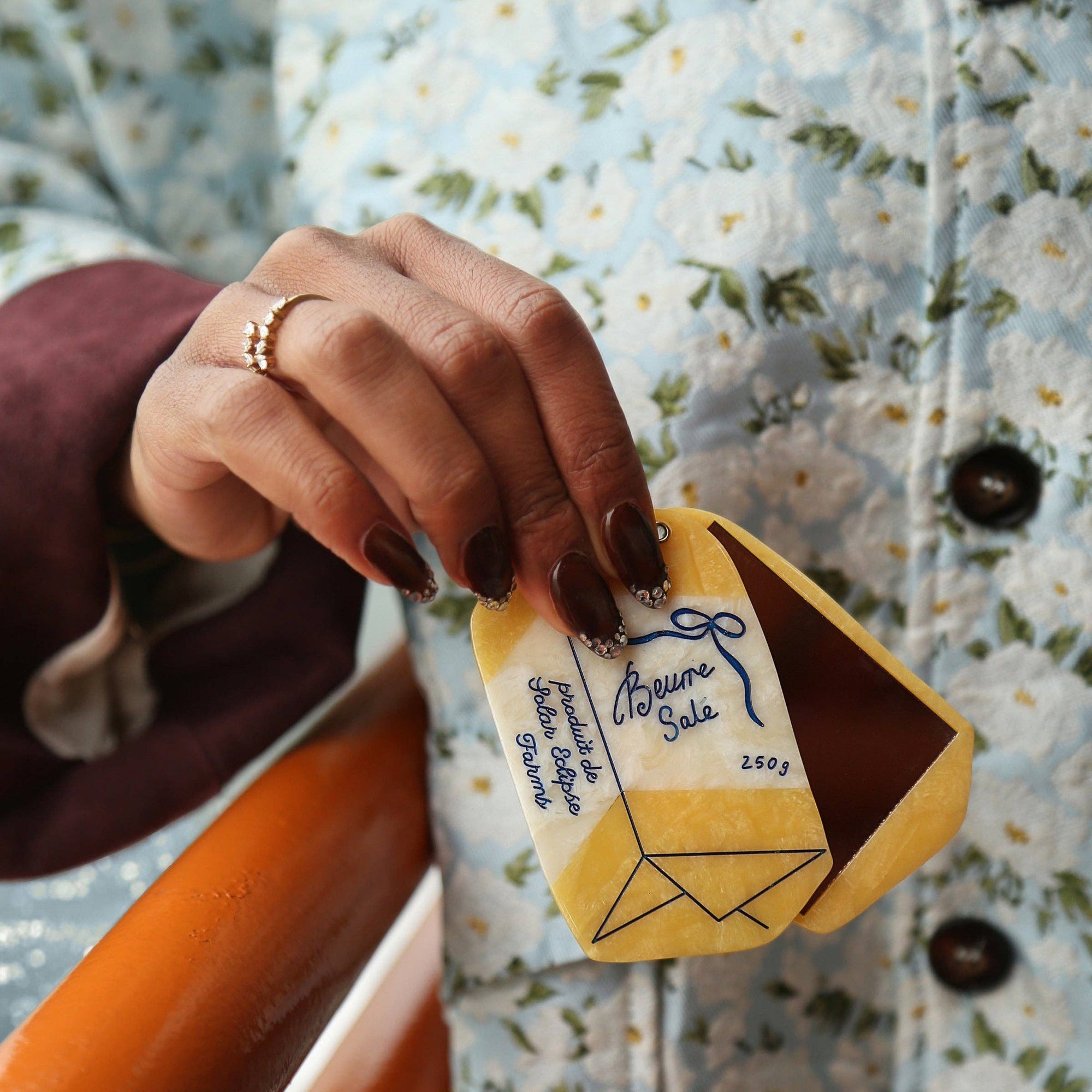 Hand holding a small yellow and brown product with a label against a floral-patterned background
