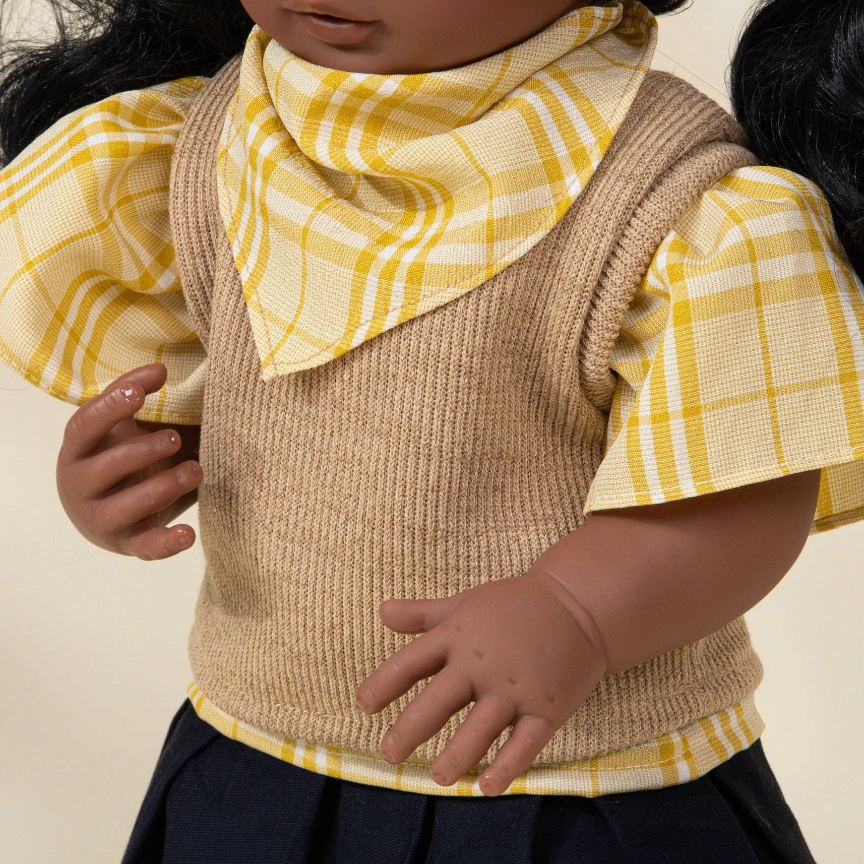 Doll wearing a yellow checkered shirt, beige vest, and navy skirt with a yellow plaid scarf.
