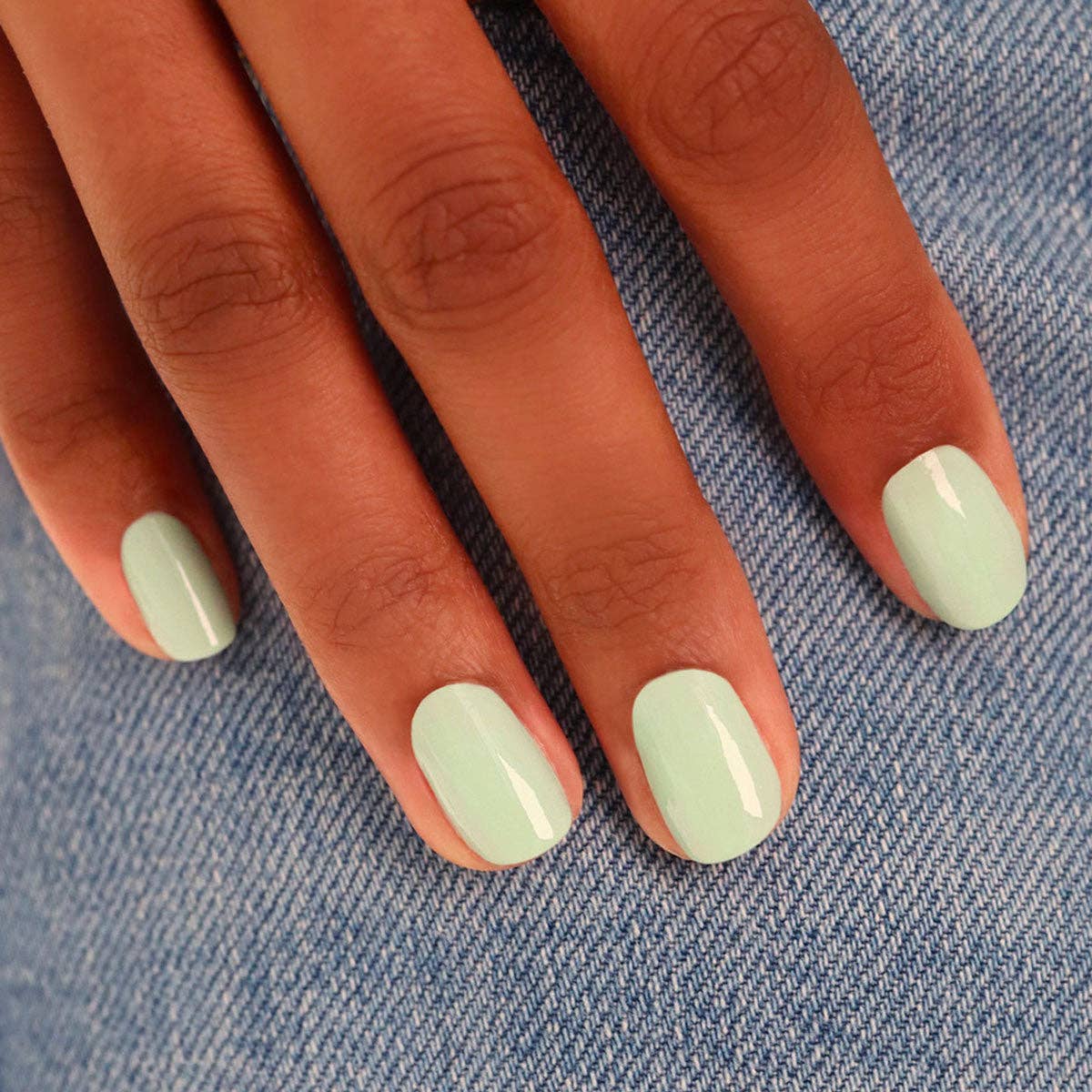 Hand with light green nail polish on a denim background