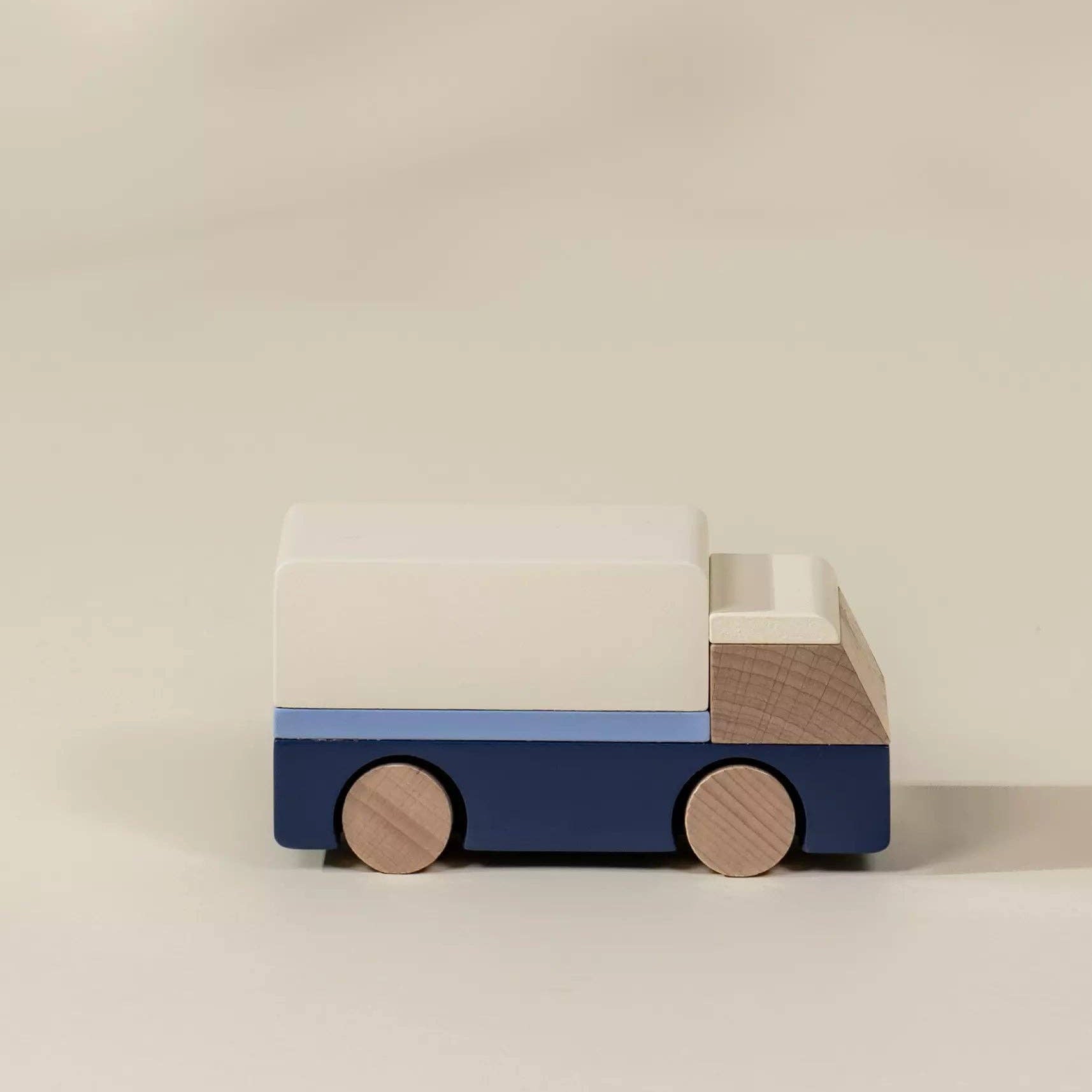 Wooden toy truck with a white top and blue and brown bottom on a beige background