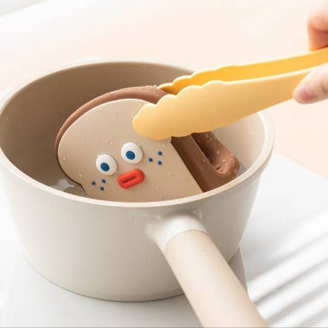 Person using a yellow spatula to an oven mitt from a pot