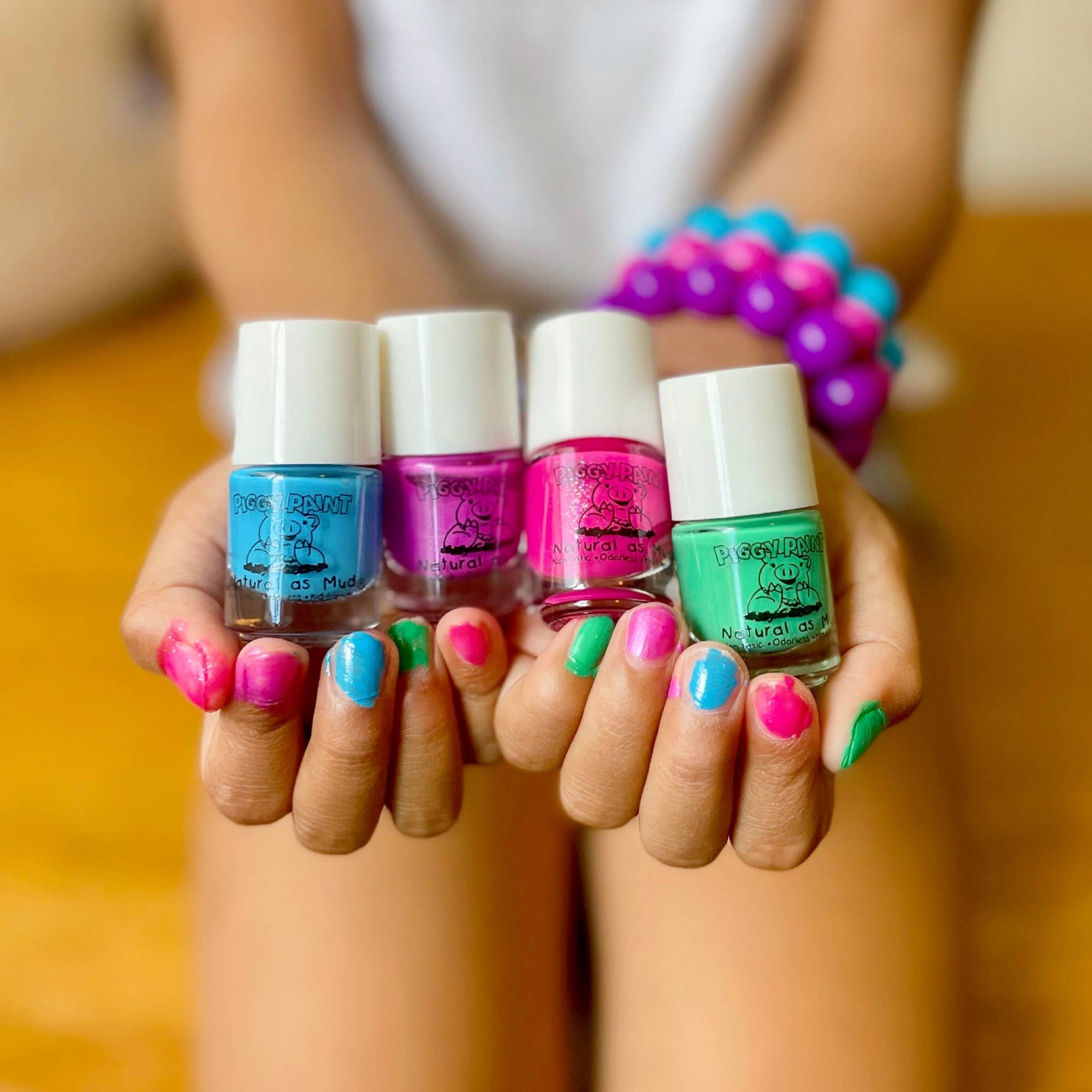 Four small bottles of nail polish held by a person with colorful nail polish on their nails.