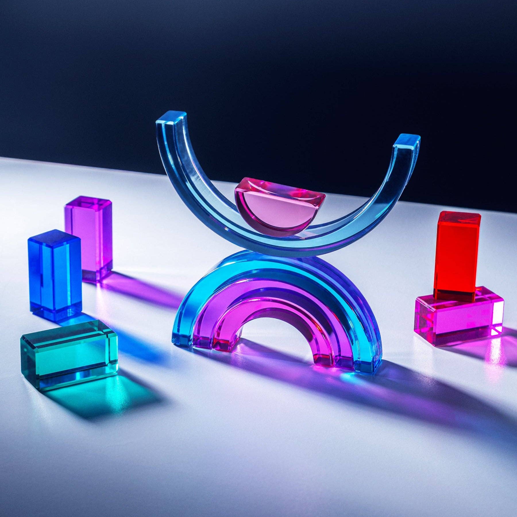 Colorful glass geometric shapes on a reflective surface with a dark background