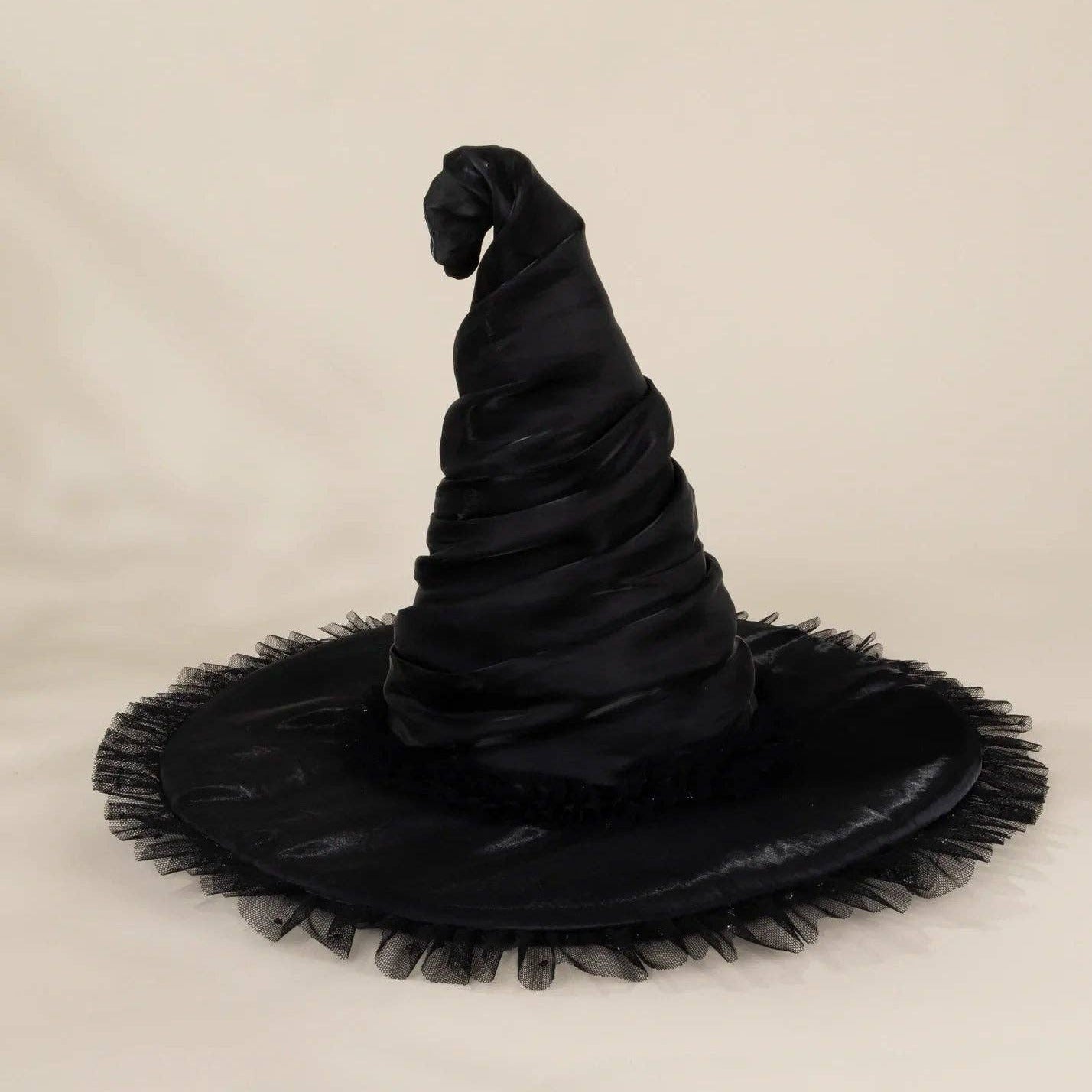 A black witch hat with a wide, frayed brim, photographed against a plain light beige studio background.