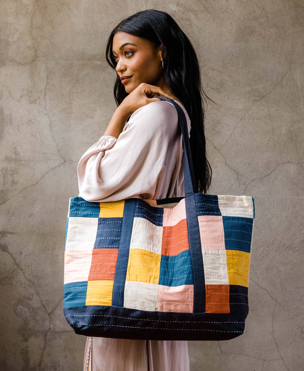 Woman carrying a colorful checkered tote bag against a textured wall.