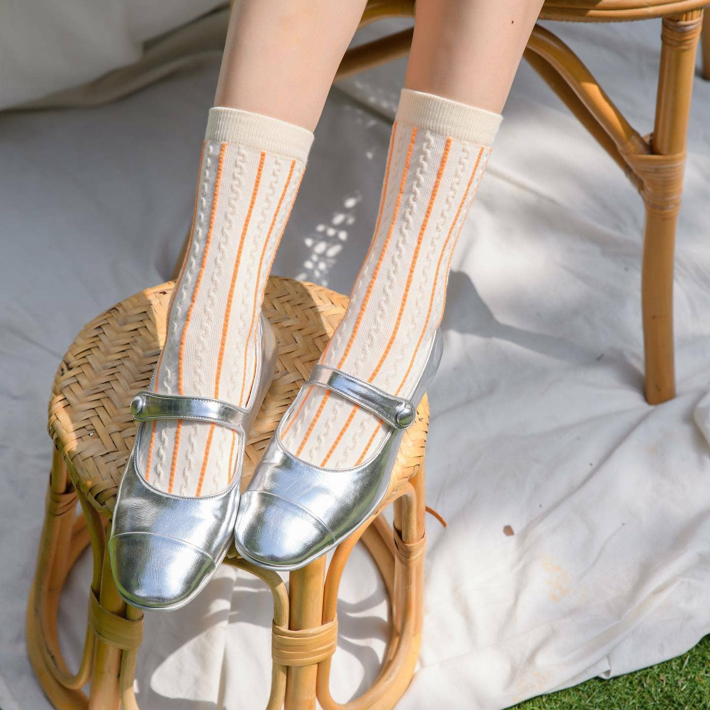 Person wearing white socks with orange stripes and clear shoes on a wicker stool.