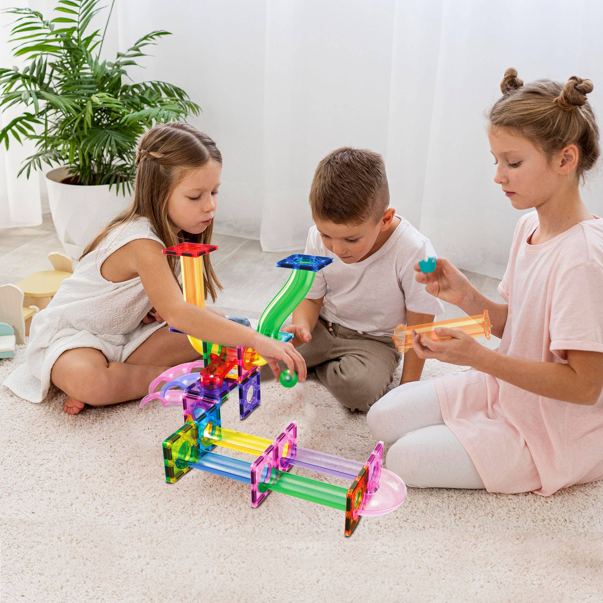 Three children playing with colorful marble run toys on a light-colored floor.