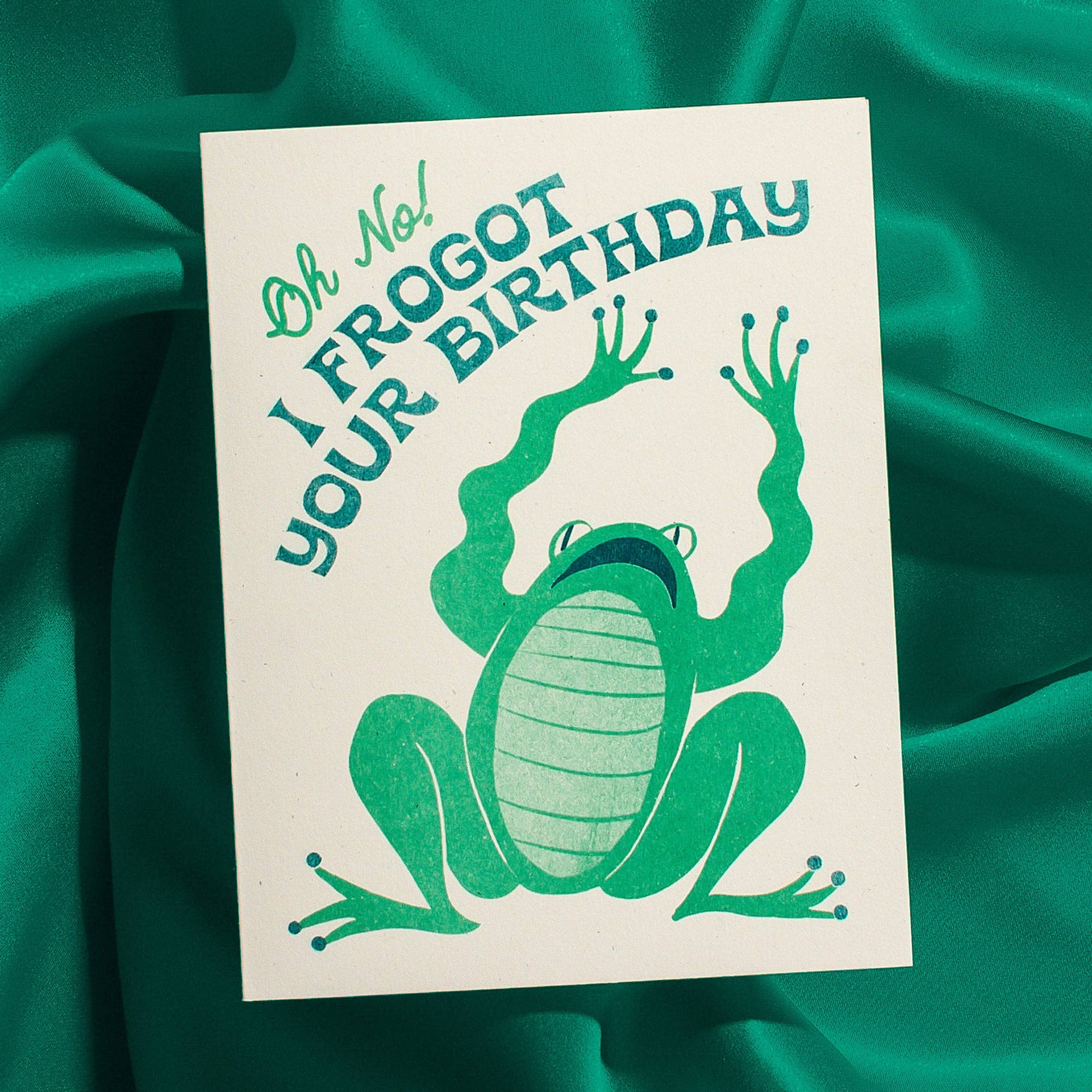 Birthday card with green frog illustration and text on a teal fabric background