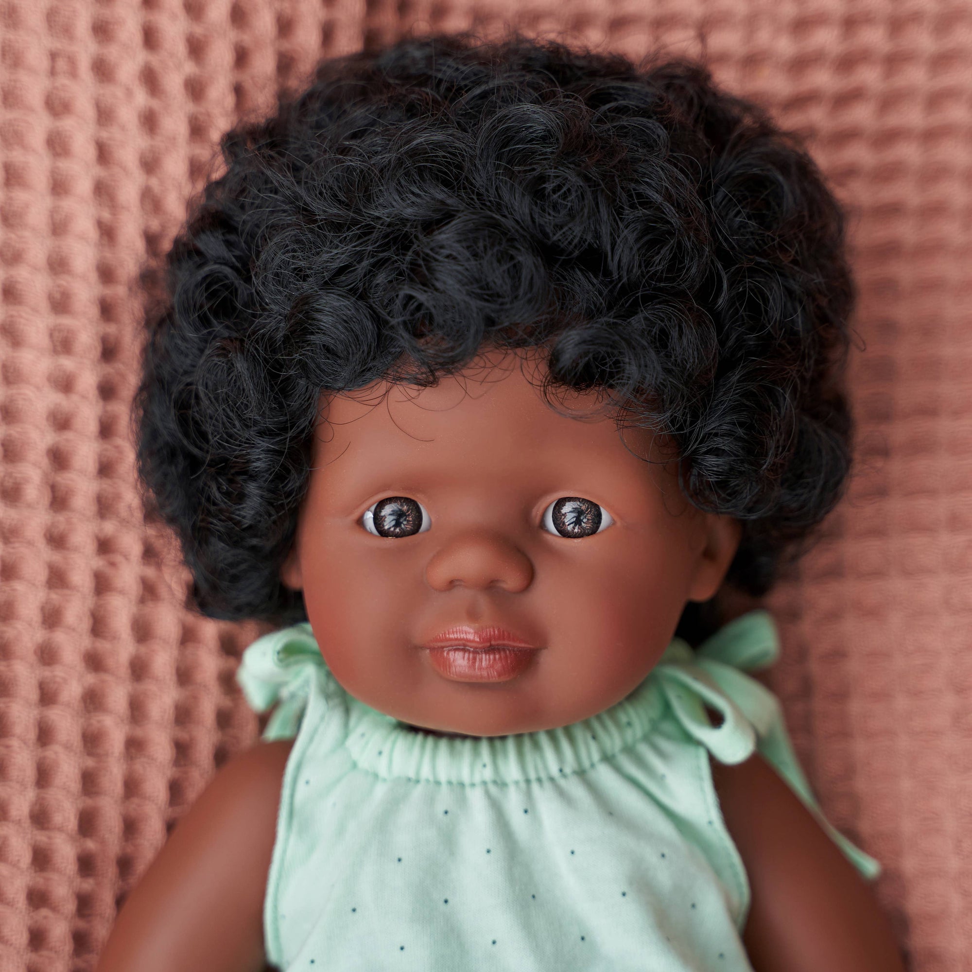 Doll with curly hair wearing a light green outfit against a pink textured background