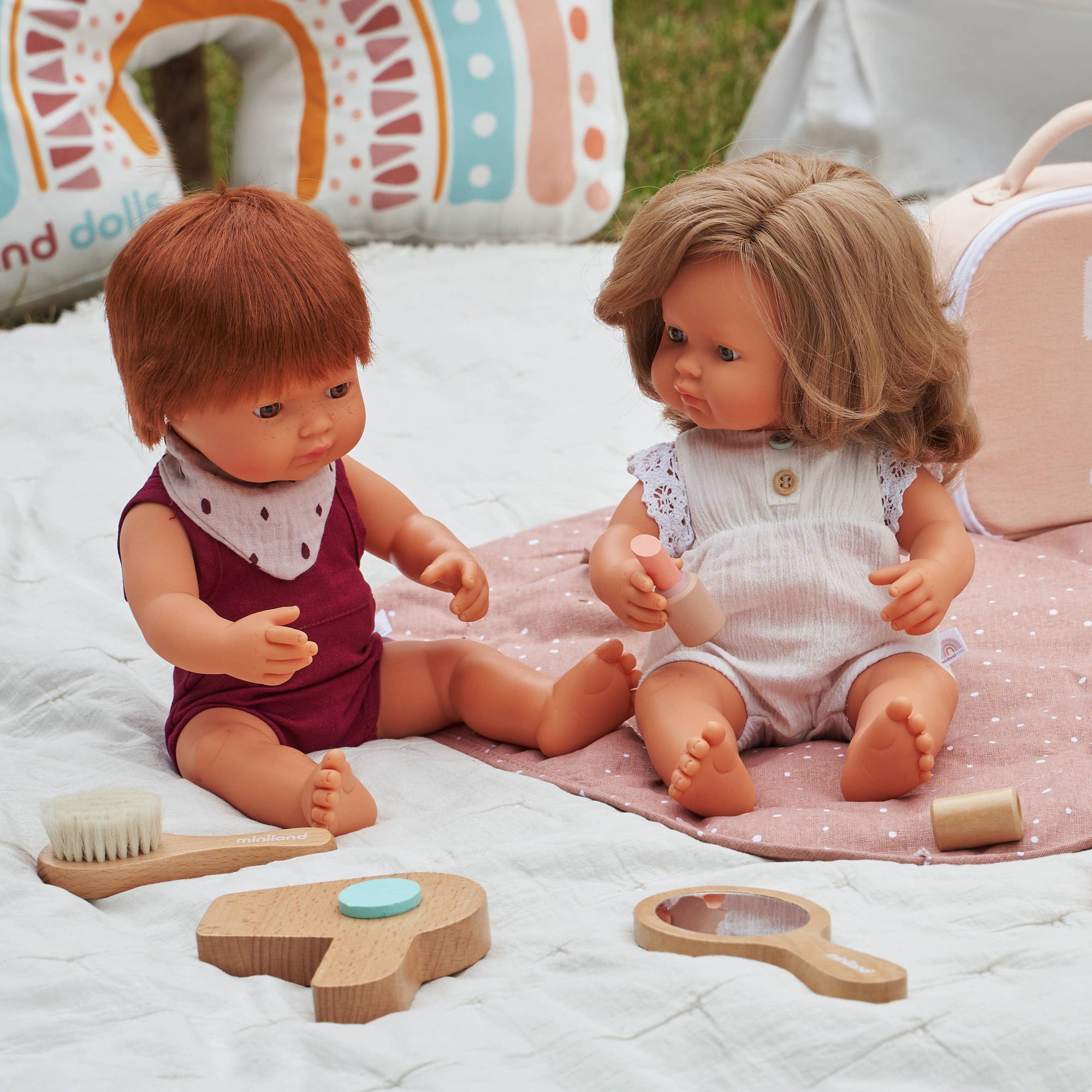 Two dolls sitting on a blanket with toys around them