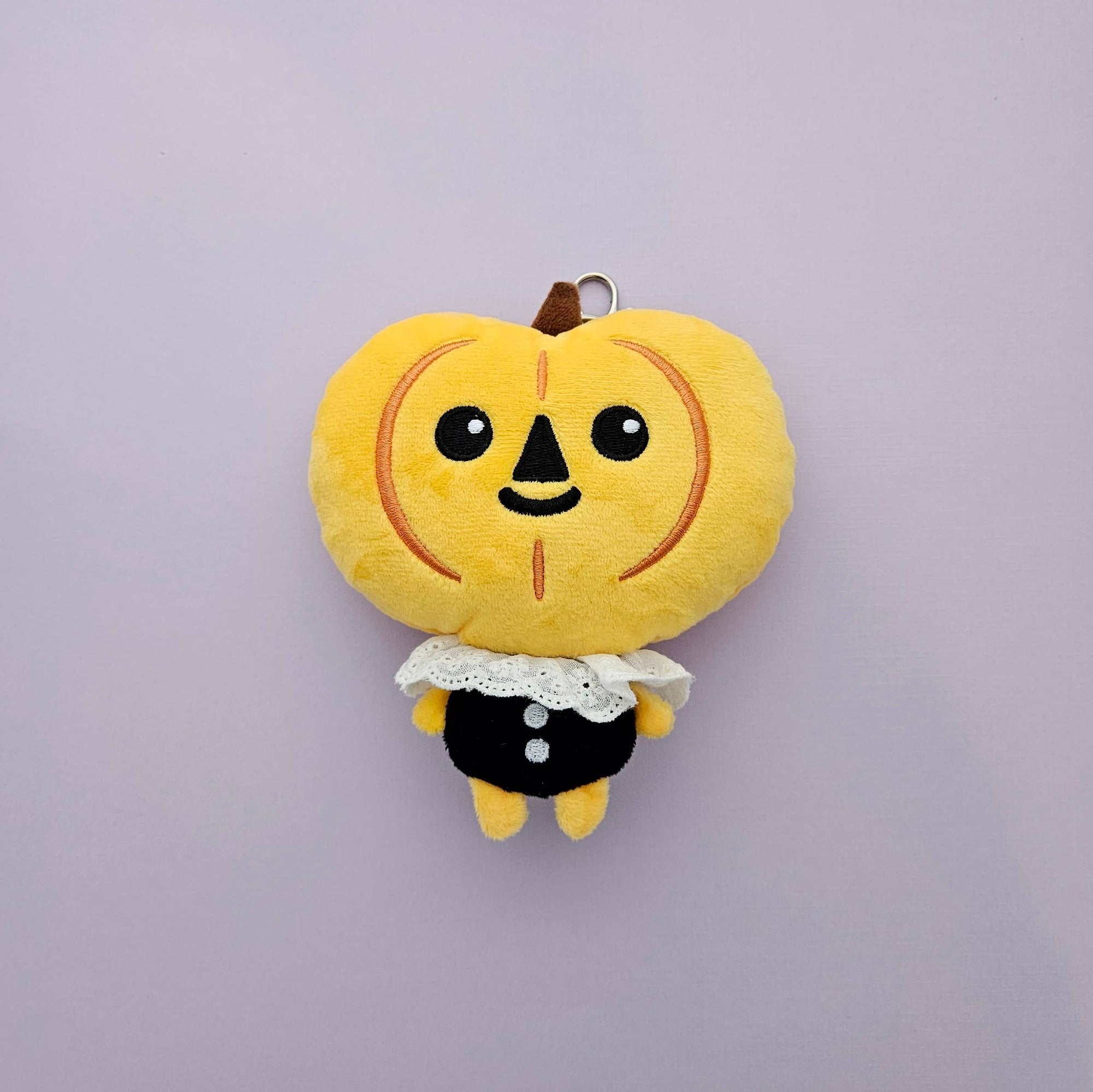 Plush toy shaped like a cartoon pumpkin with a face on a light purple background