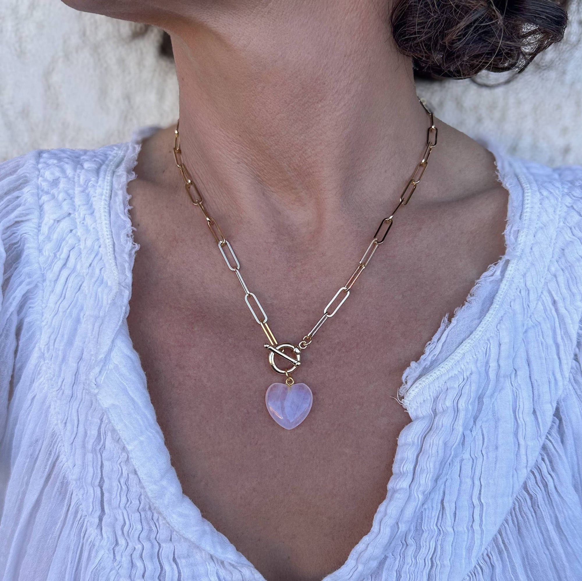 Necklace with a heart-shaped pendant worn by a person in a white textured top.