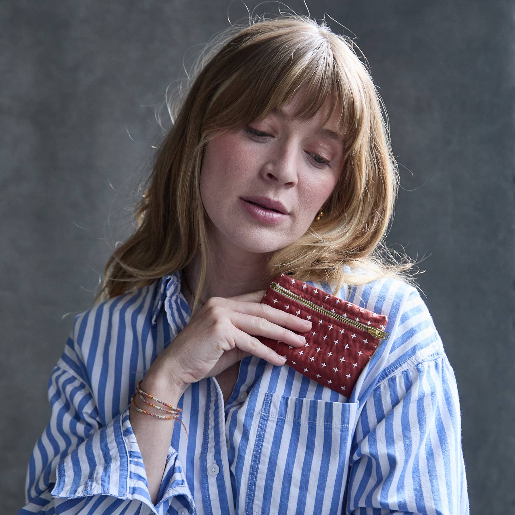 Woman holding a red wallet with white polka dots against a gray background