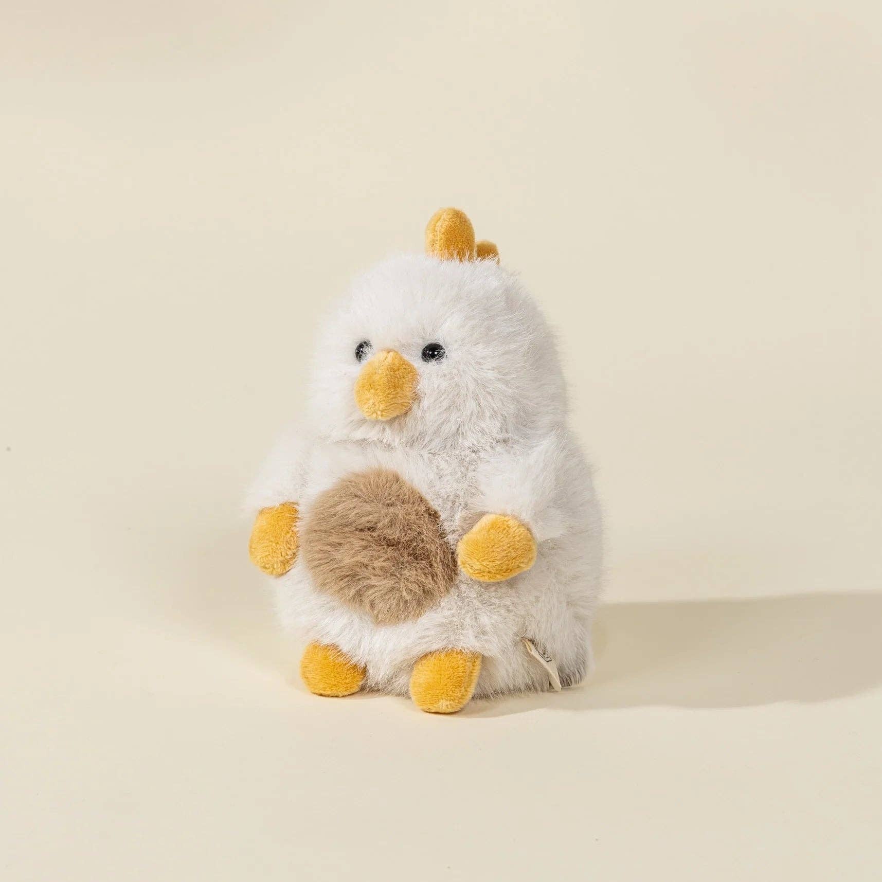 Plush toy chick with a fluffy brown bottom on a beige background