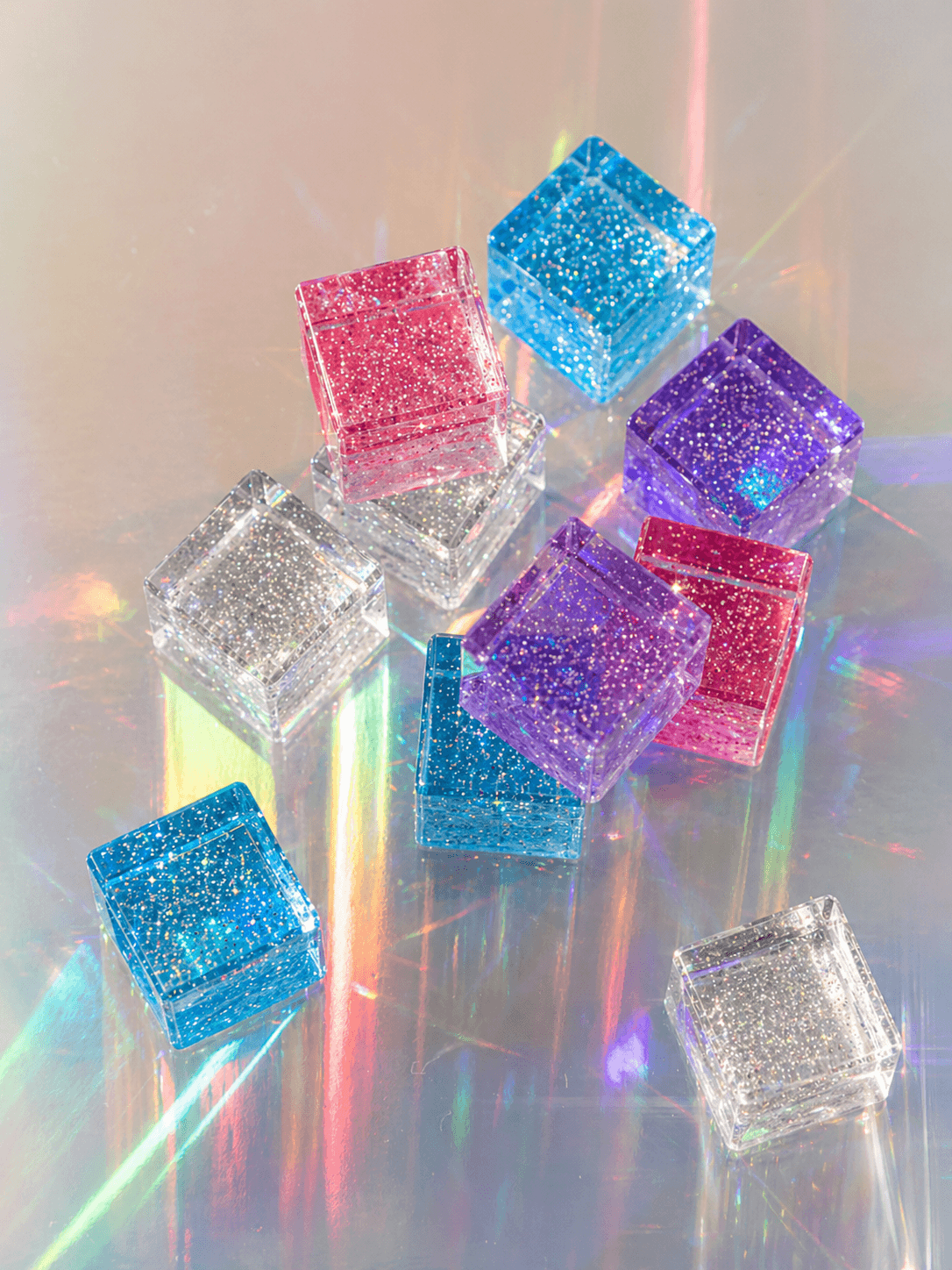 Colorful glittery cube-shaped objects on a reflective surface with rainbows
