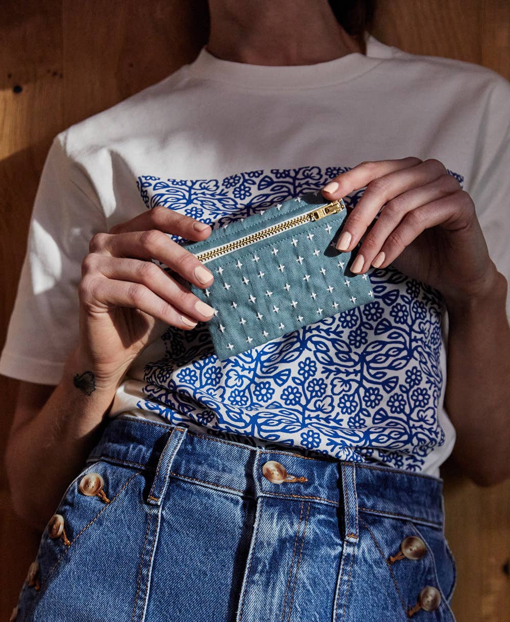 Person holding a blue clutch with white patterns against a wooden background