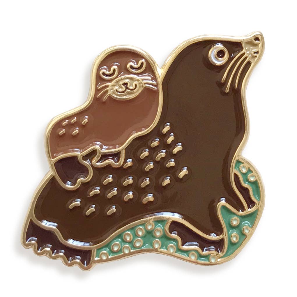 Brown seal-shaped enamel pin with gold and green accents on a white background