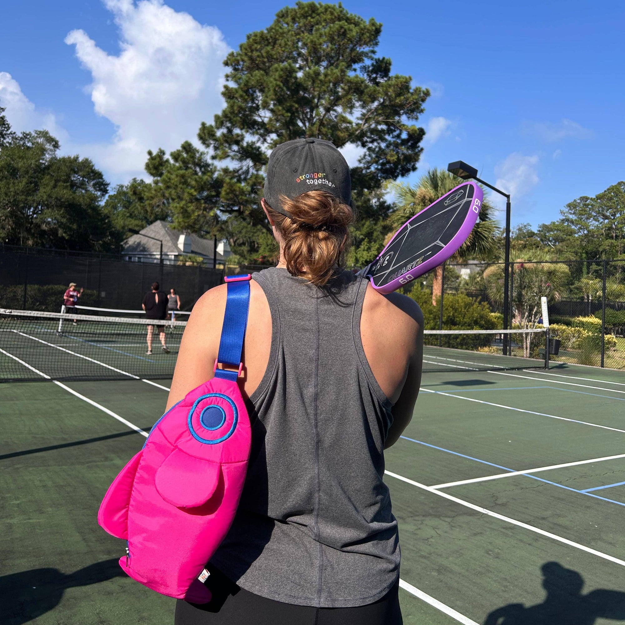 Person with a pink bag and purple tennis racket on a tennis court