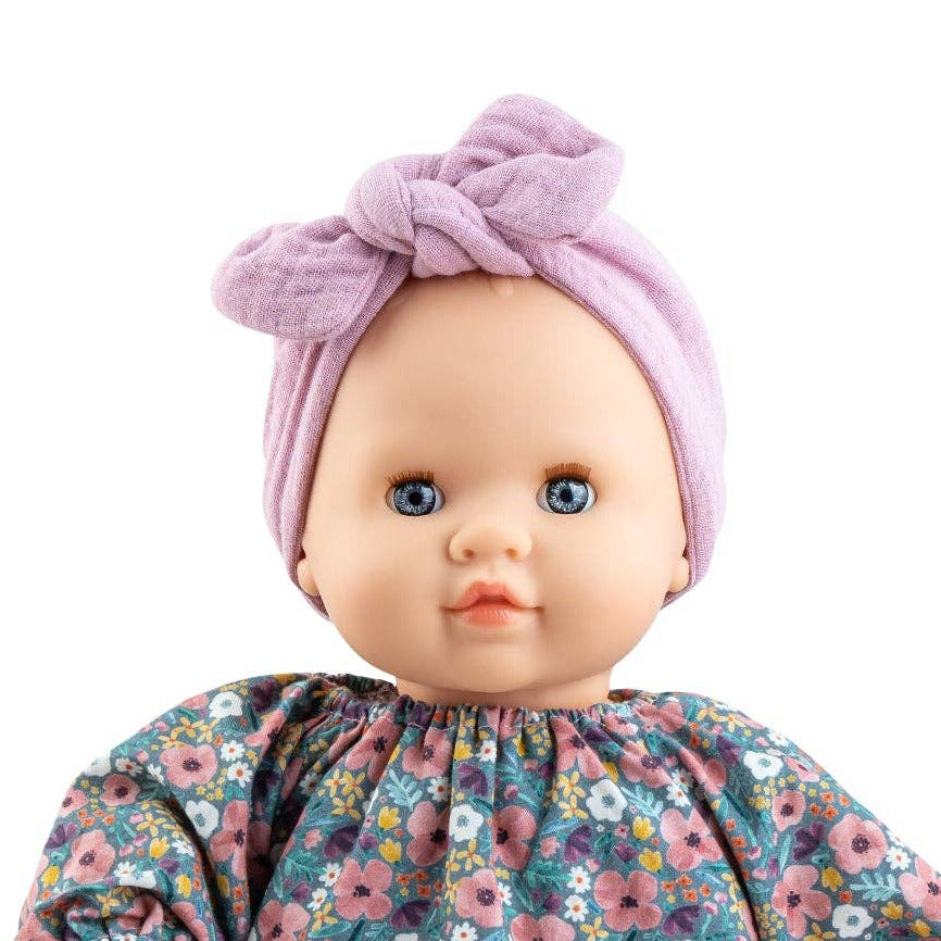 A baby doll with a purple knotted headband, a long-sleeve floral dress, and beige knit tights, isolated on a white background.