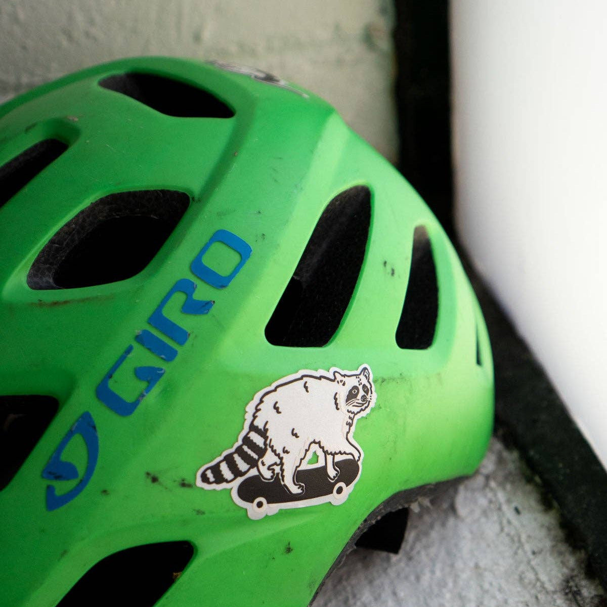 Green Giro helmet with a raccoon sticker on a concrete surface
