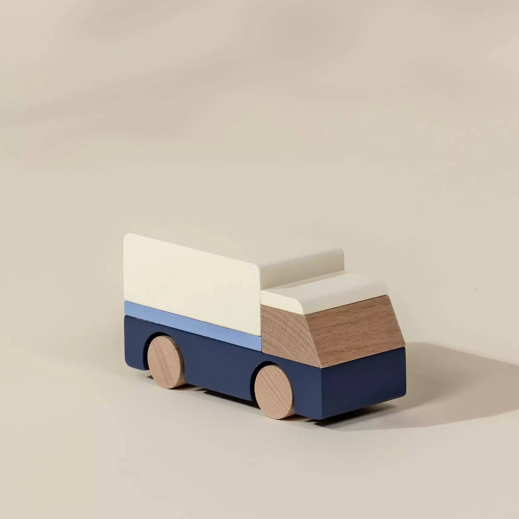 Wooden toy truck with a blue base, white top, and brown wheels on a beige background