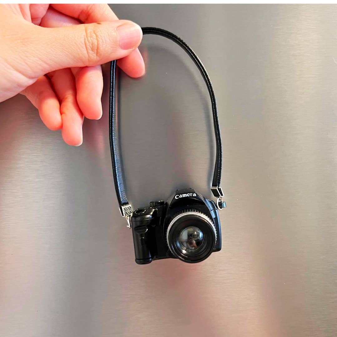 Camera with a strap held by a hand on a metallic surface