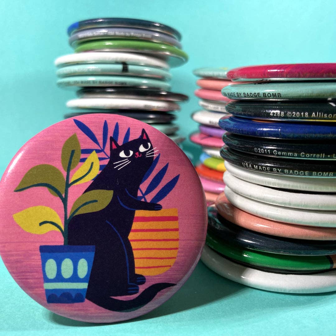 Button badge with a black cat design on a pink background, surrounded by other colorful buttons.