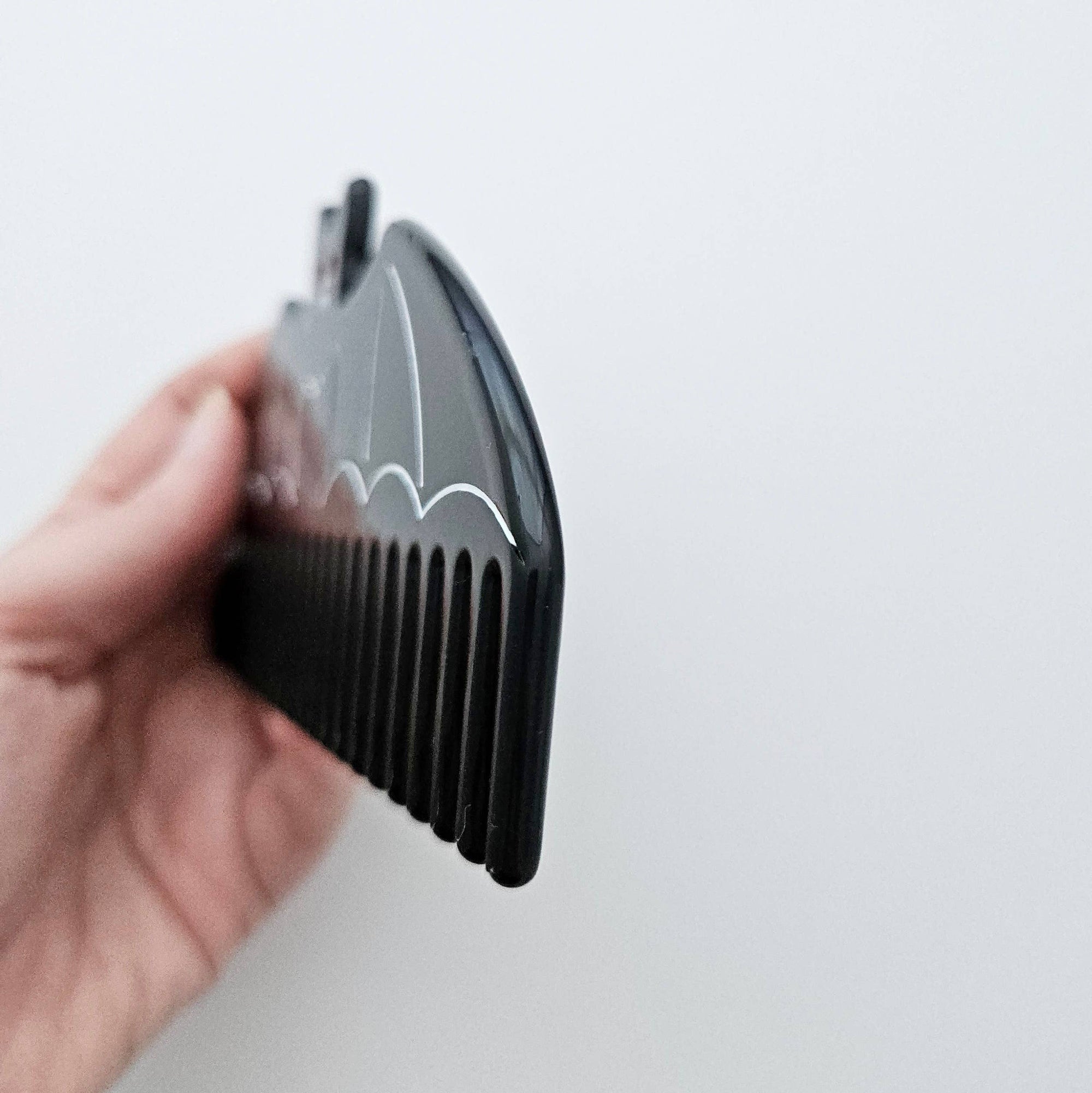 Black comb held by a hand against a light gray background