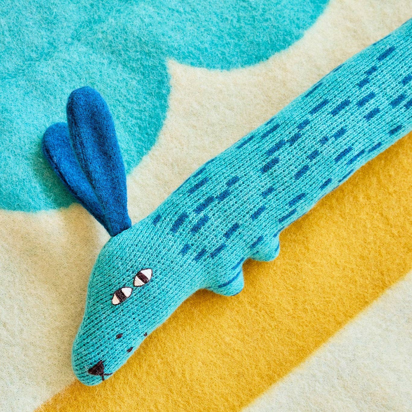 Blue knitted toy resembling a dog on a colorful striped background