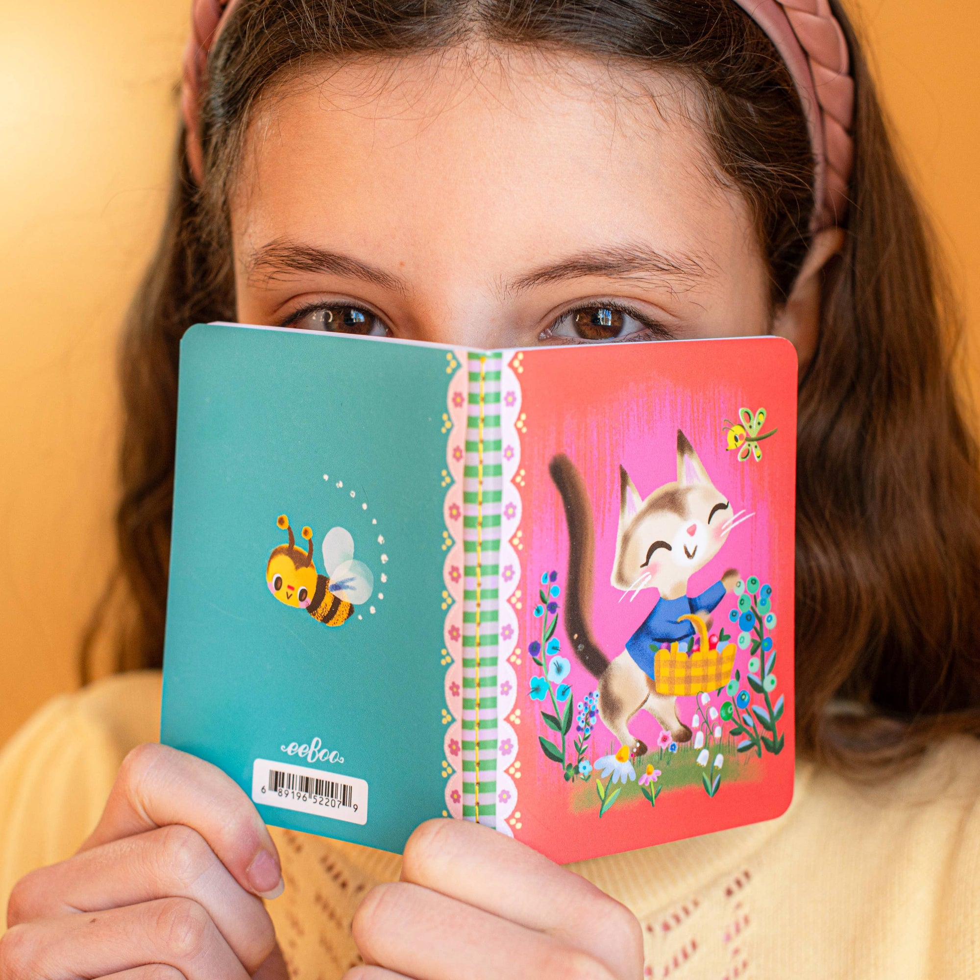 Girl holding a colorful notebook with cartoon designs against a yellow background