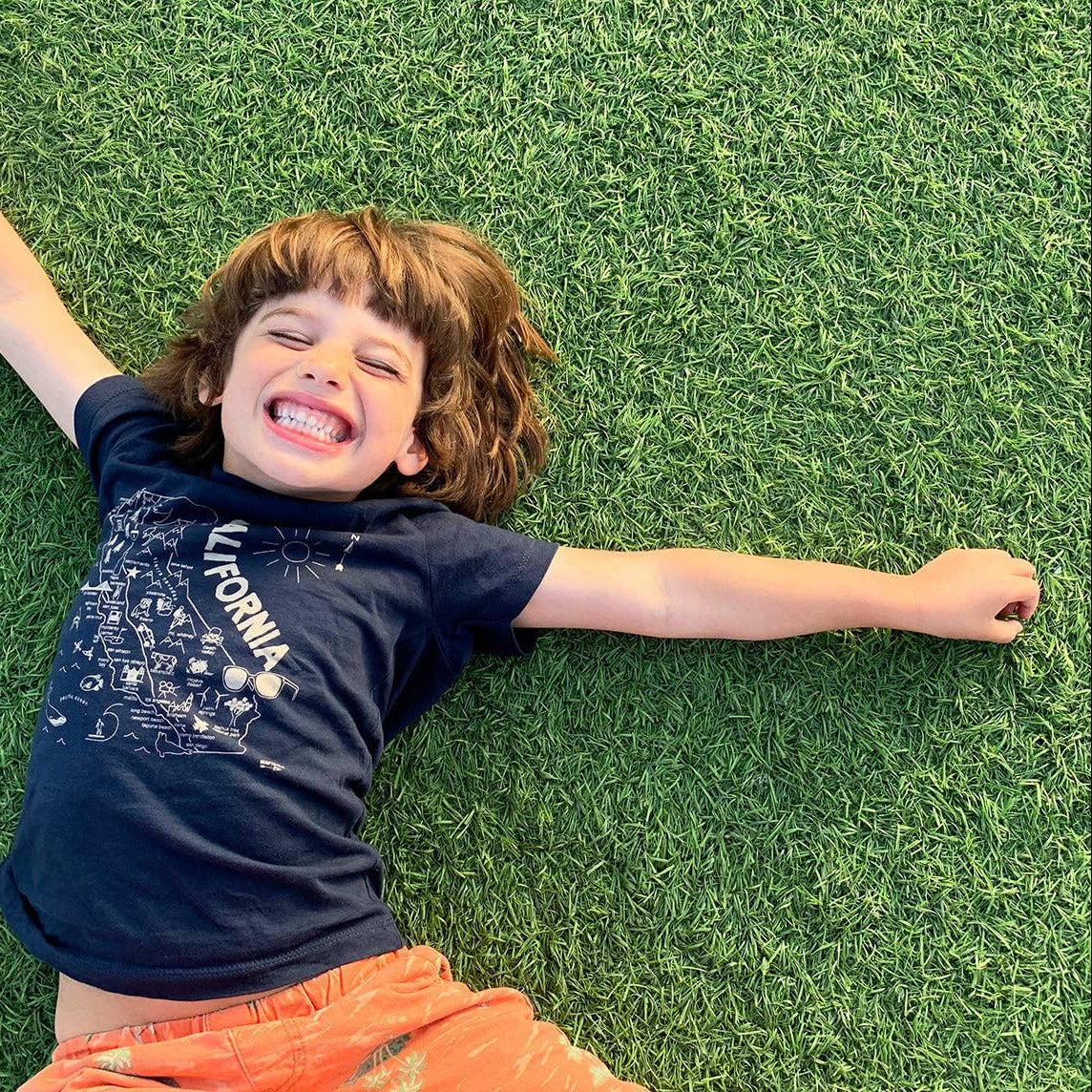 Child lying on grass wearing a blue shirt with 'California' print