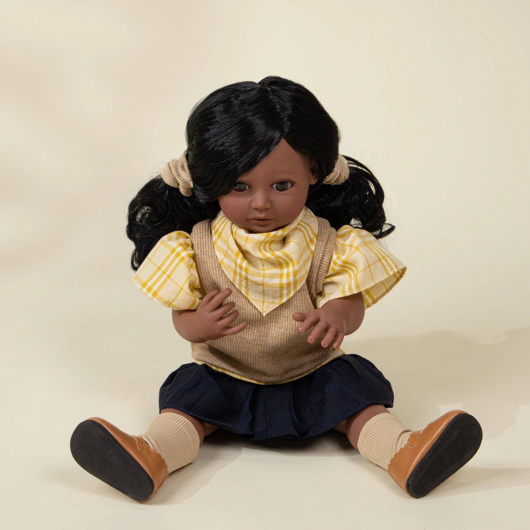 Doll with black hair styled in pigtails, wearing a yellow checkered shirt and brown vest on a beige background.