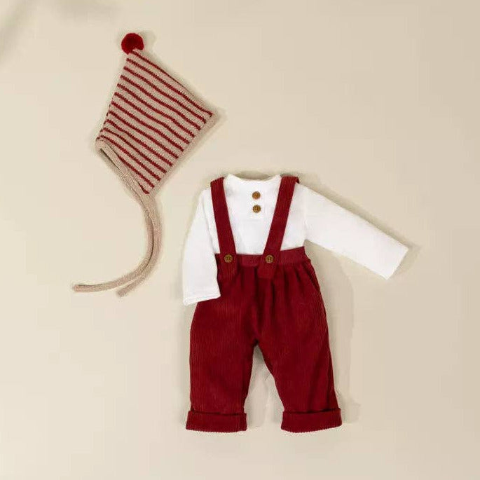 Children's outfit with red pants, white shirt, and striped hat on a beige background