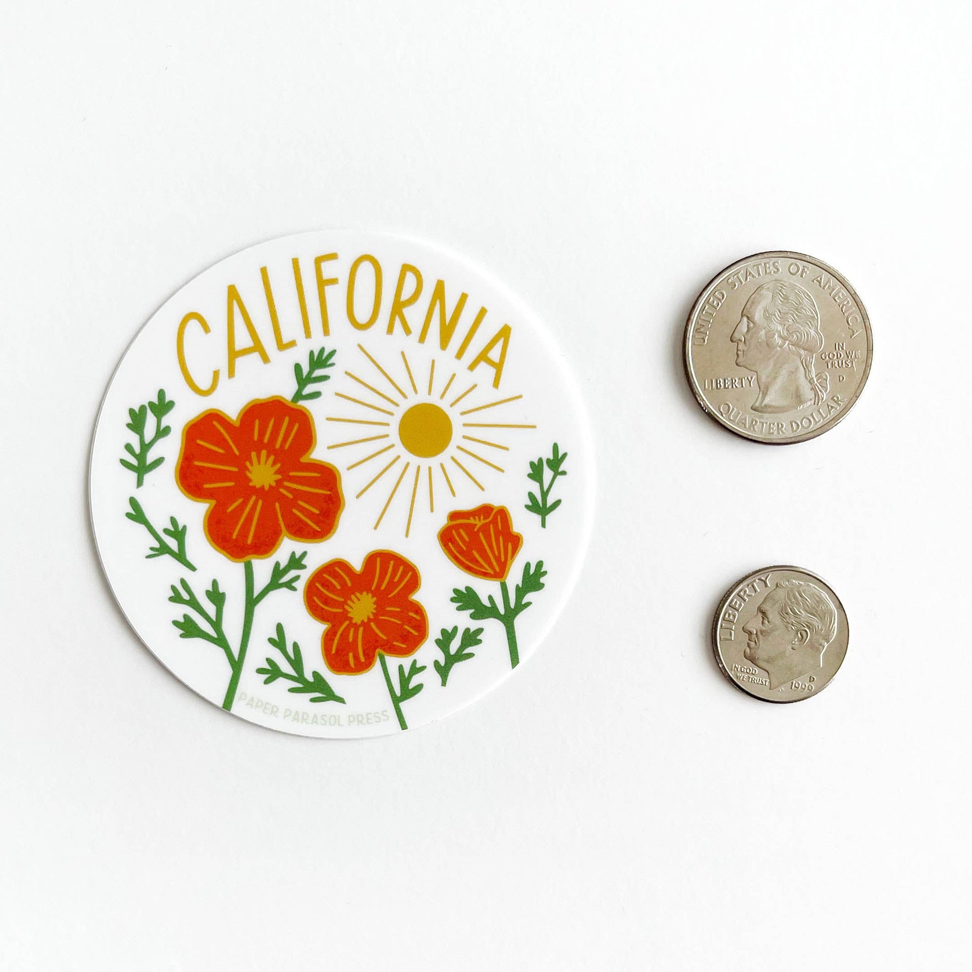 Circular sticker with California text and floral design next to two coins on a white background