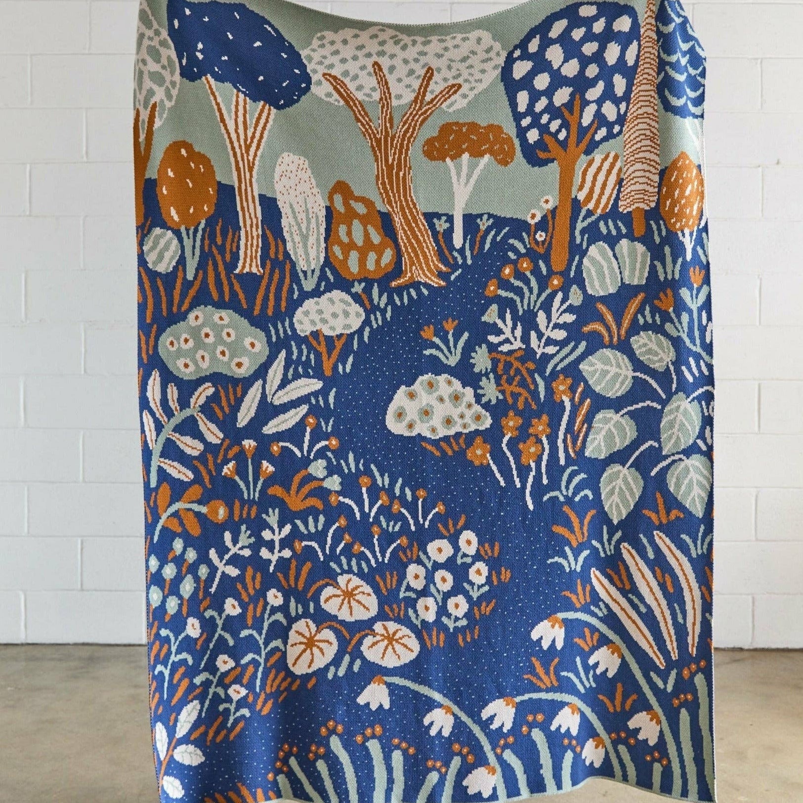 Colorful forest-themed blanket draped over a person against a white brick wall.