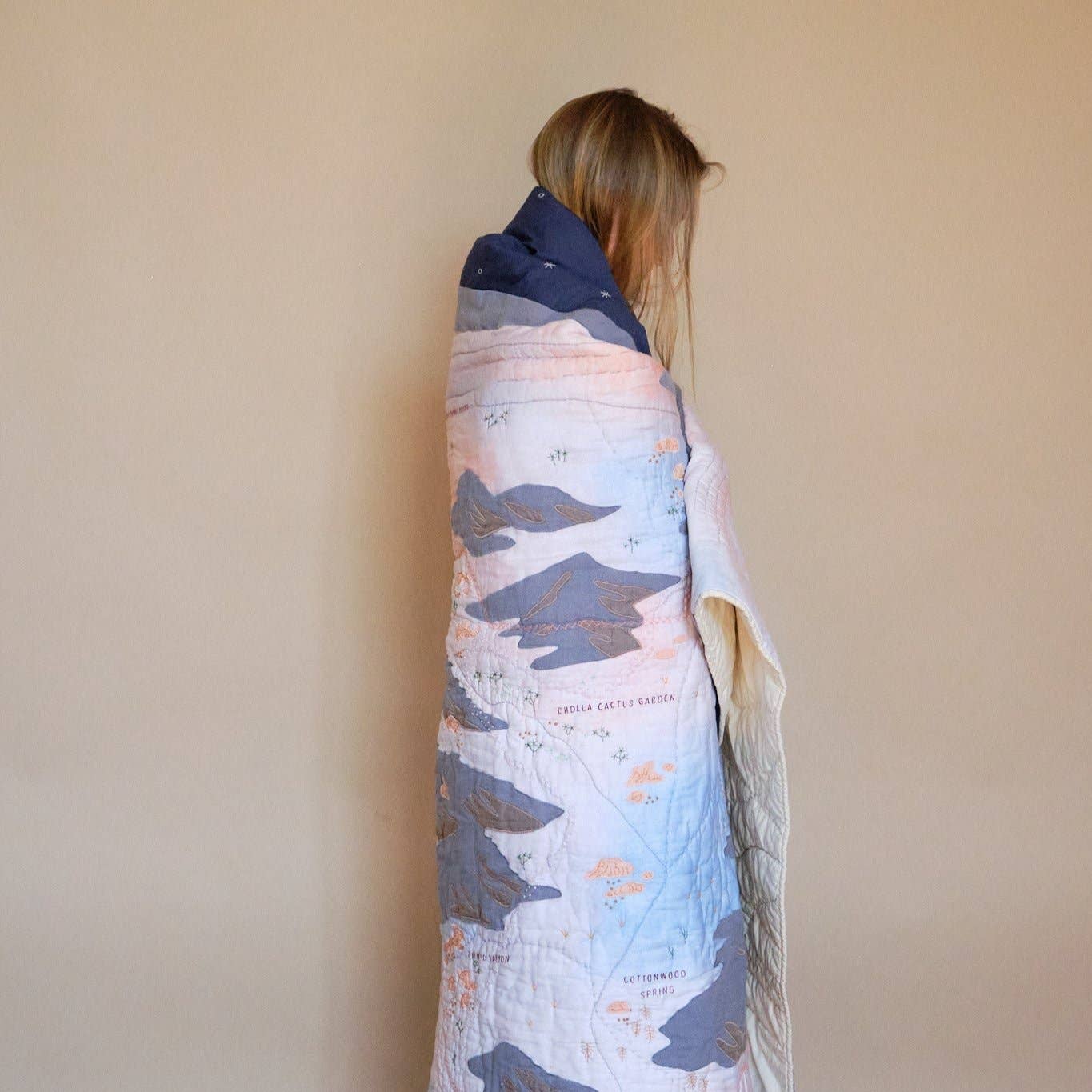 Person wrapped in a colorful quilt with a neutral background