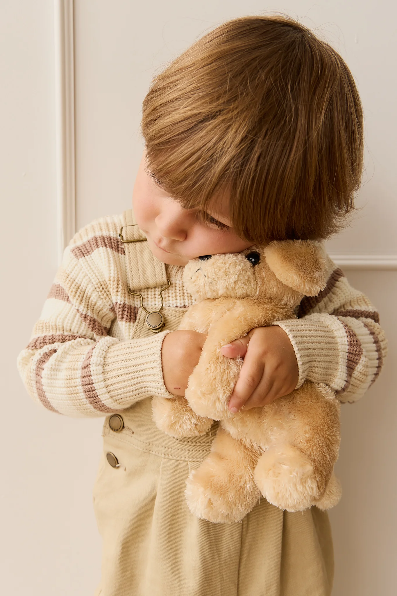 Child holding a teddy bear against a neutral background