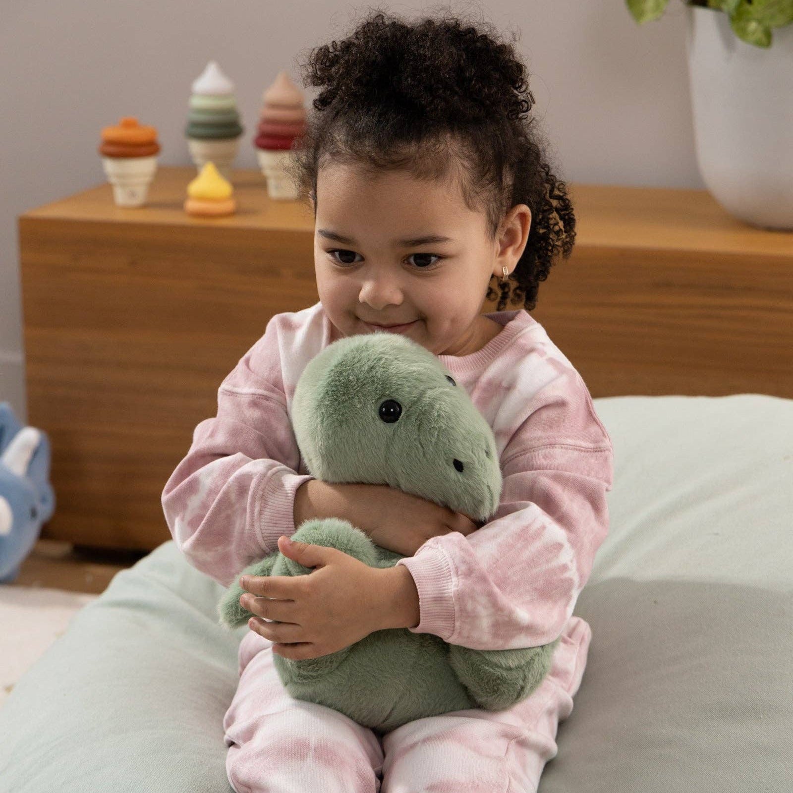 Child holding a green plush toy on a bean bag chair with a neutral background