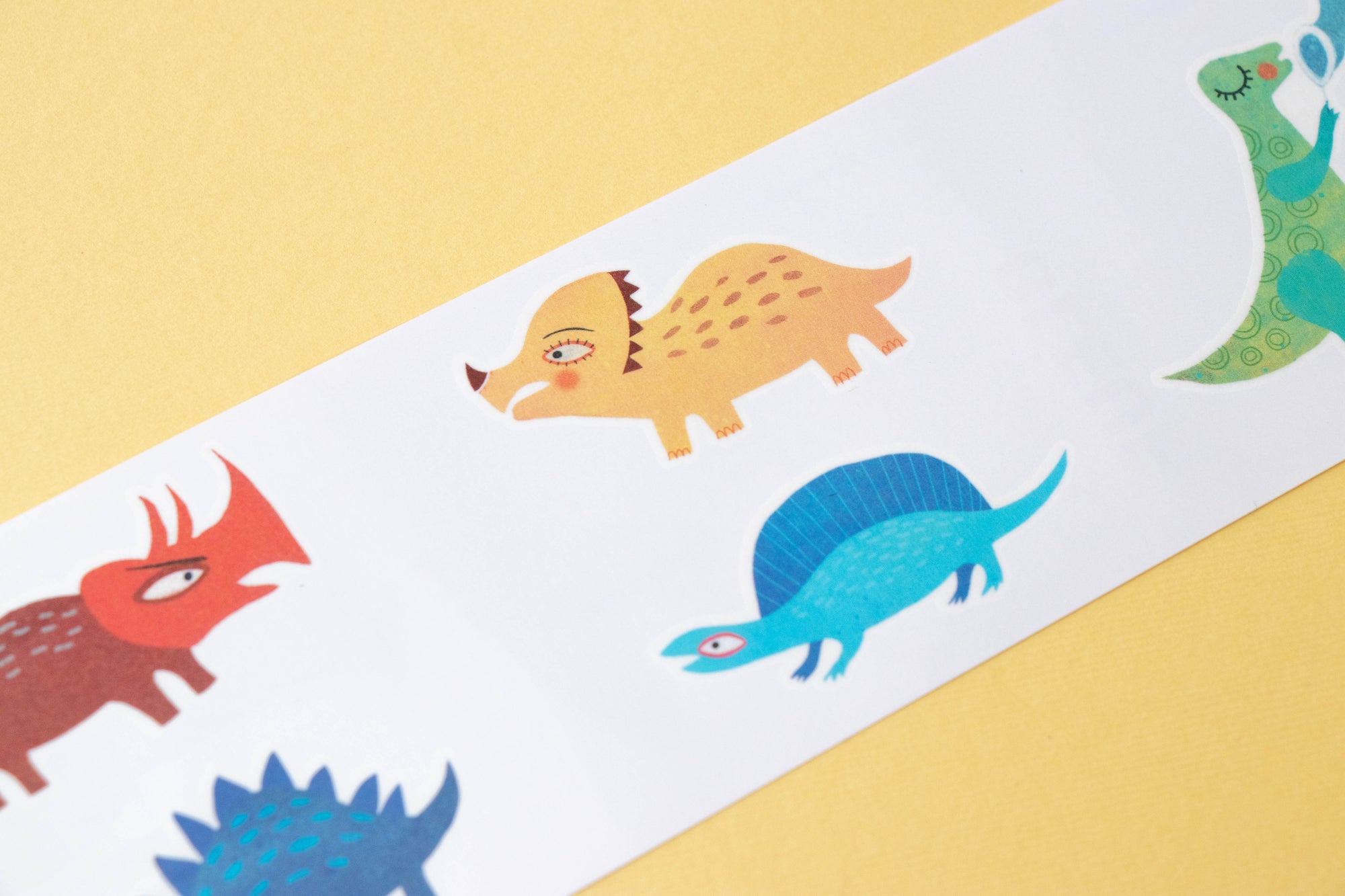 Colorful dinosaur tattoo's on a white strip with a yellow background