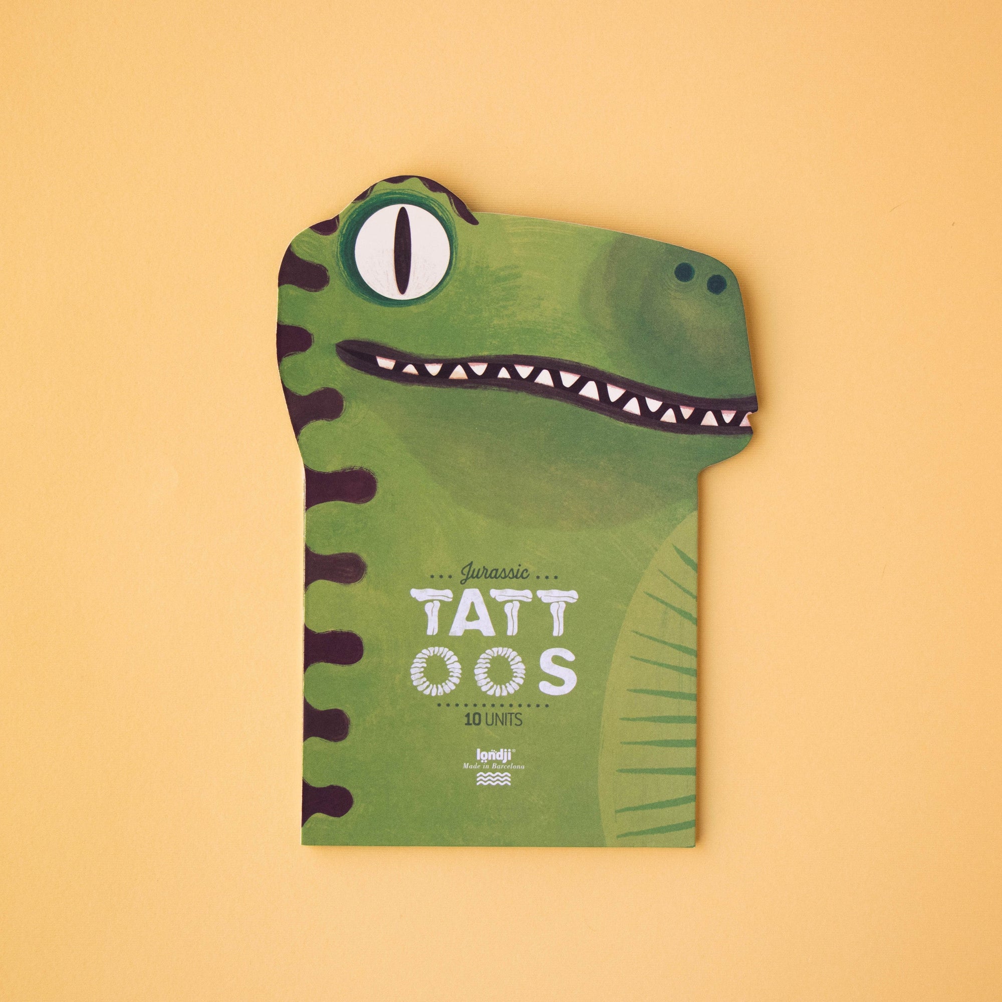 Green dinosaur-shaped book with 'TATT OOS' text on a beige background