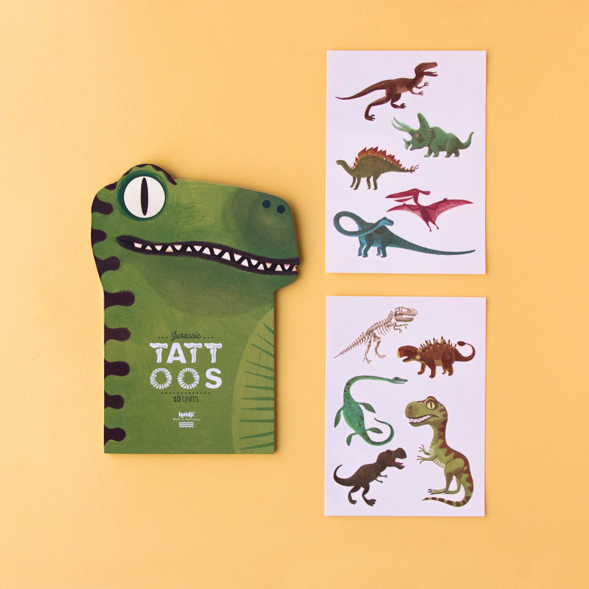 Green dinosaur-themed tattoo book and sheets on a yellow background