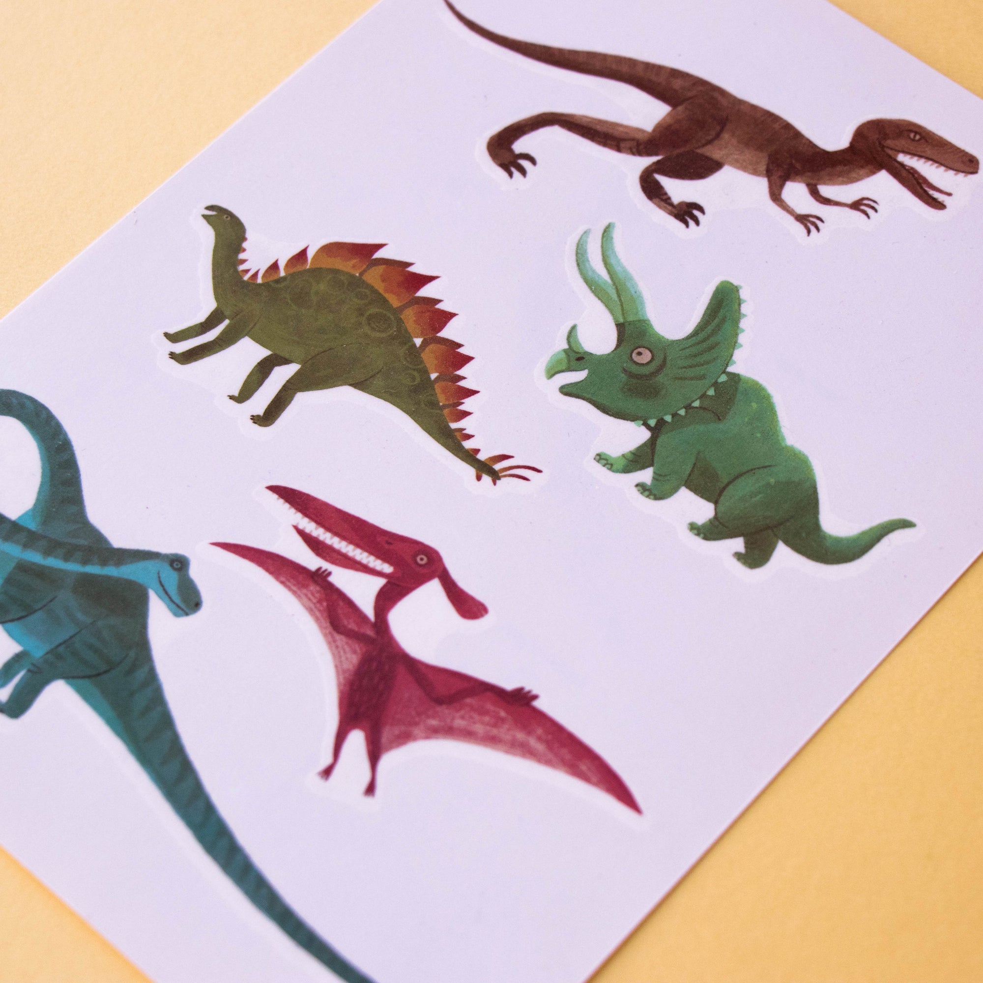 Colorful dinosaur illustrations on a white sheet of paper with a yellow background