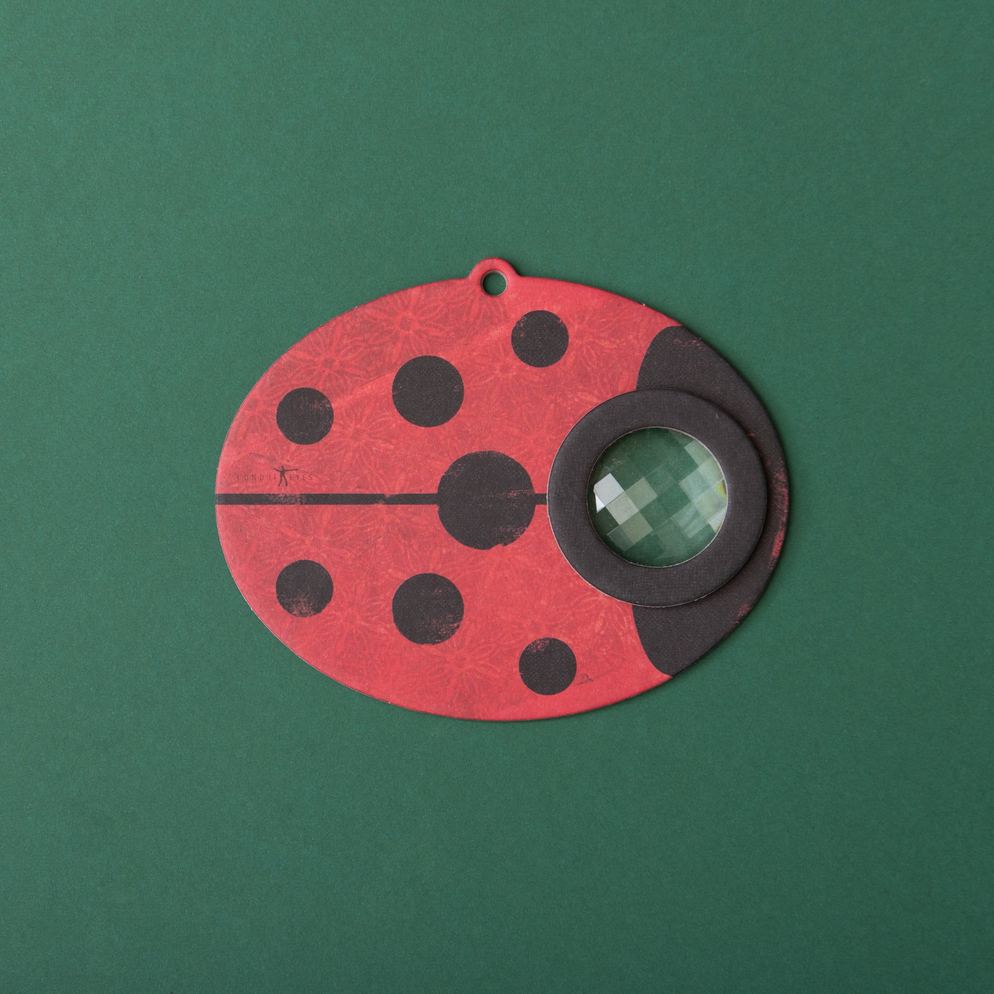 Red ladybug-shaped Kaleidoscope with black spots on a green background